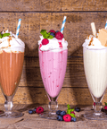 Three tall milkshakes: chocolate, strawberry, and vanilla, topped with whipped cream, berries, and honeycomb syrup.