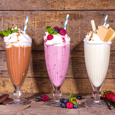 Three tall milkshakes: chocolate, strawberry, and vanilla, topped with whipped cream, berries, and honeycomb syrup.