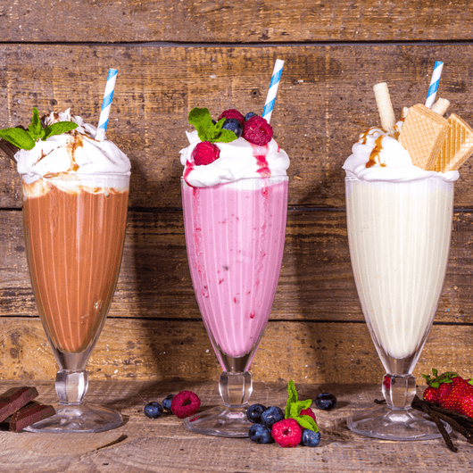 Three tall milkshakes: chocolate, strawberry, and vanilla, topped with whipped cream, berries, and honeycomb syrup.